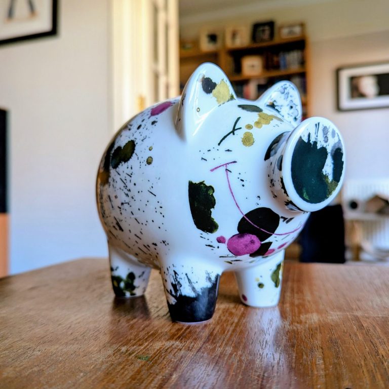 Nothing is expensive when it gives you value. A piggy bank stood on a table. It's mainly white with a paint splatter design and a wide smile.