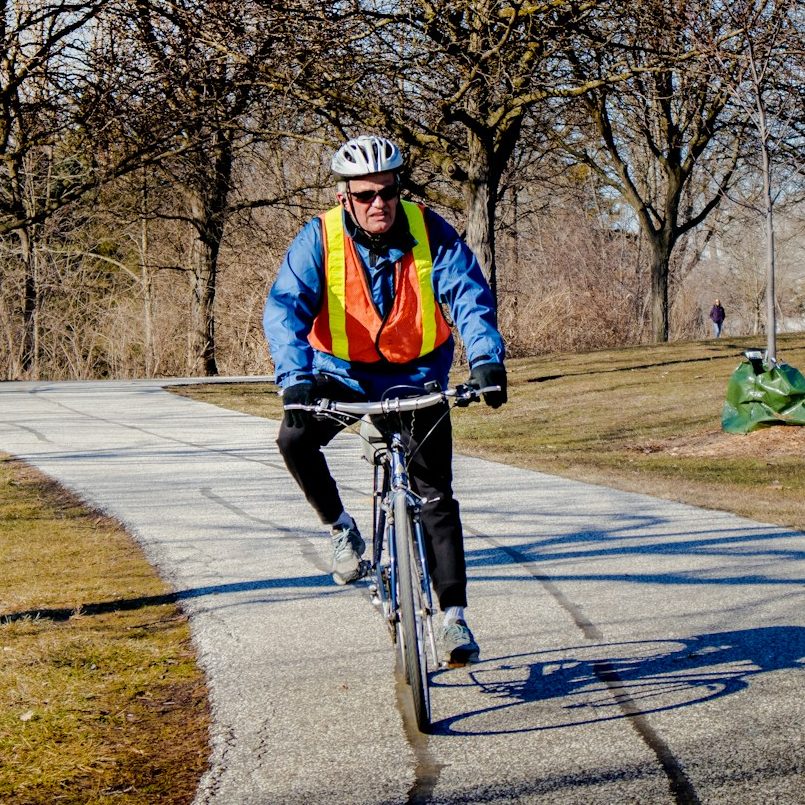 A cyclist wearing hi-vis clothing, riding through a park.