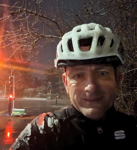 It doesn't have to be good weather to be a great ride! A selfie of Simon Owen, it's dark, the roads are wet, he has snow on his bike helmet and jacket, plus a smile on his face.