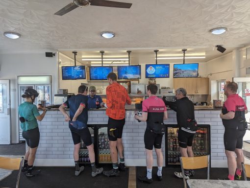 Chippy 6 cyclists in summer kit waiting at a chip shop counter in Hornsea, mid 200 mile ride.
